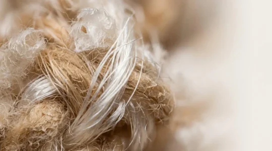 Dettaglio macro di fibre di cashmere e seta intrecciate che mostrano la struttura naturale e la qualità dei materiali pregiati